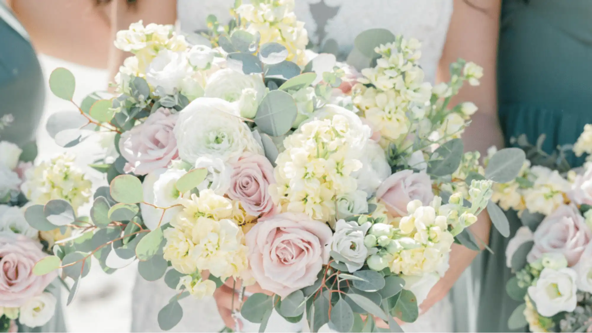 Bridal bouquet with delicate pink roses, white ranunculus, pale yellow accent flowers, and silver dollar eucalyptus